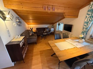 A cozy living area with a wooden ceiling, a sofa, a dining table, and a TV mounted on the wall. - Apartment in Bramberg am Wildkogel With Balcony (Bramberg am Wildkogel)