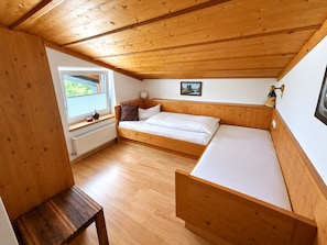 Ein Zimmer mit Holzbalkendecke, einem Bett mit weißer Bettwäsche, einem kleinen Tisch und einem Fenster mit Blick auf Grünflächen.
