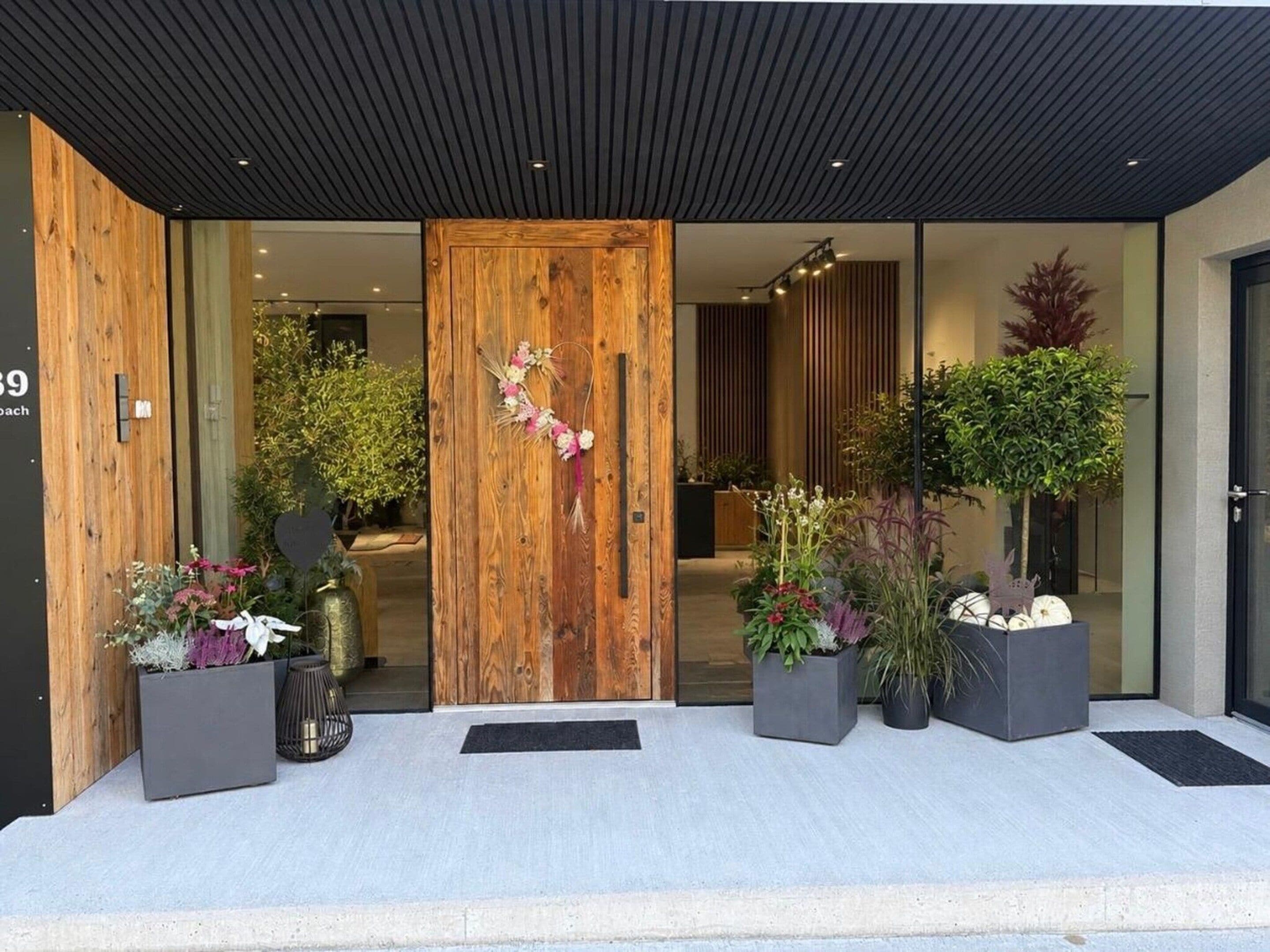 A modern building entrance with a wooden door, potted plants, and a black awning.