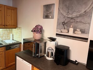 Une cuisine équipée d’un lave-vaisselle Bosch, d’une machine à café, d ’une cafetière noire et d’un vase rose orné de fleurs, posé sur le comptoir.