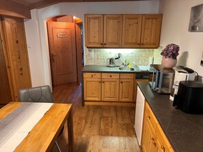 A compact kitchen with wooden cabinets, a built-in sink, and a dining area with a table. - Apartment in Bramberg am Wildkogel With Balcony (Bramberg am Wildkogel)