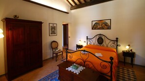 A bedroom with a wooden wardrobe, a bed with an orange bedspread, a chair, a small table with a lamp, and a painting on the wall. - Farmhouse With Pool in an Area With History, Nature and art (Bagnoregio)