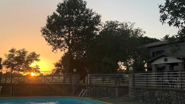 A swimming pool with a stone wall and metal railing, surrounded by trees and a building with a stone facade. - Farmhouse With Pool in an Area With History, Nature and art (Bagnoregio)