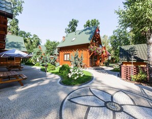 Une cabane en bois avec un toit vert, entourée d’un jardin dont le tracé circulaire est fait de pierres.