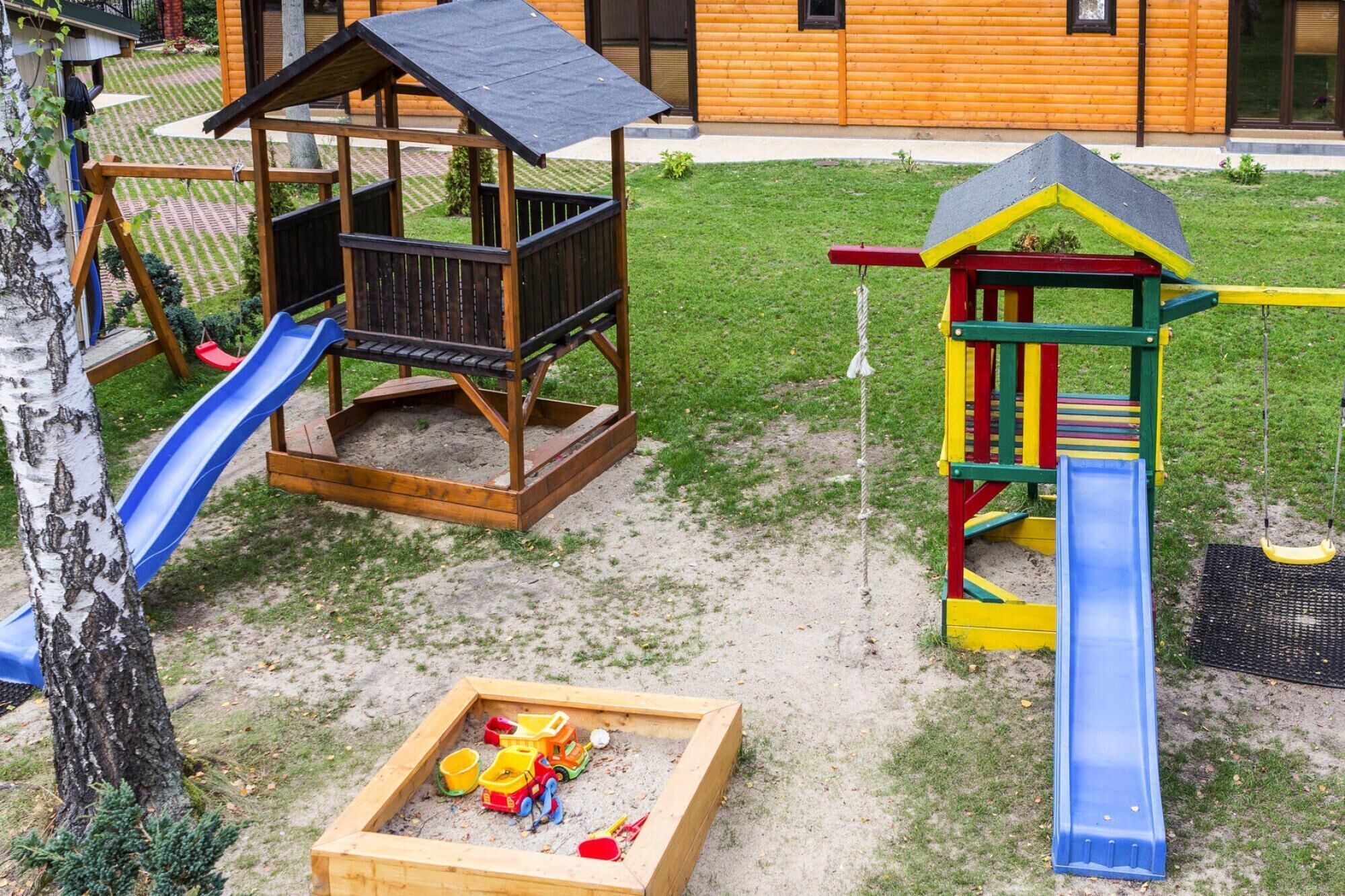 A playground with a wooden playhouse, slides, and a sandpit with toys.