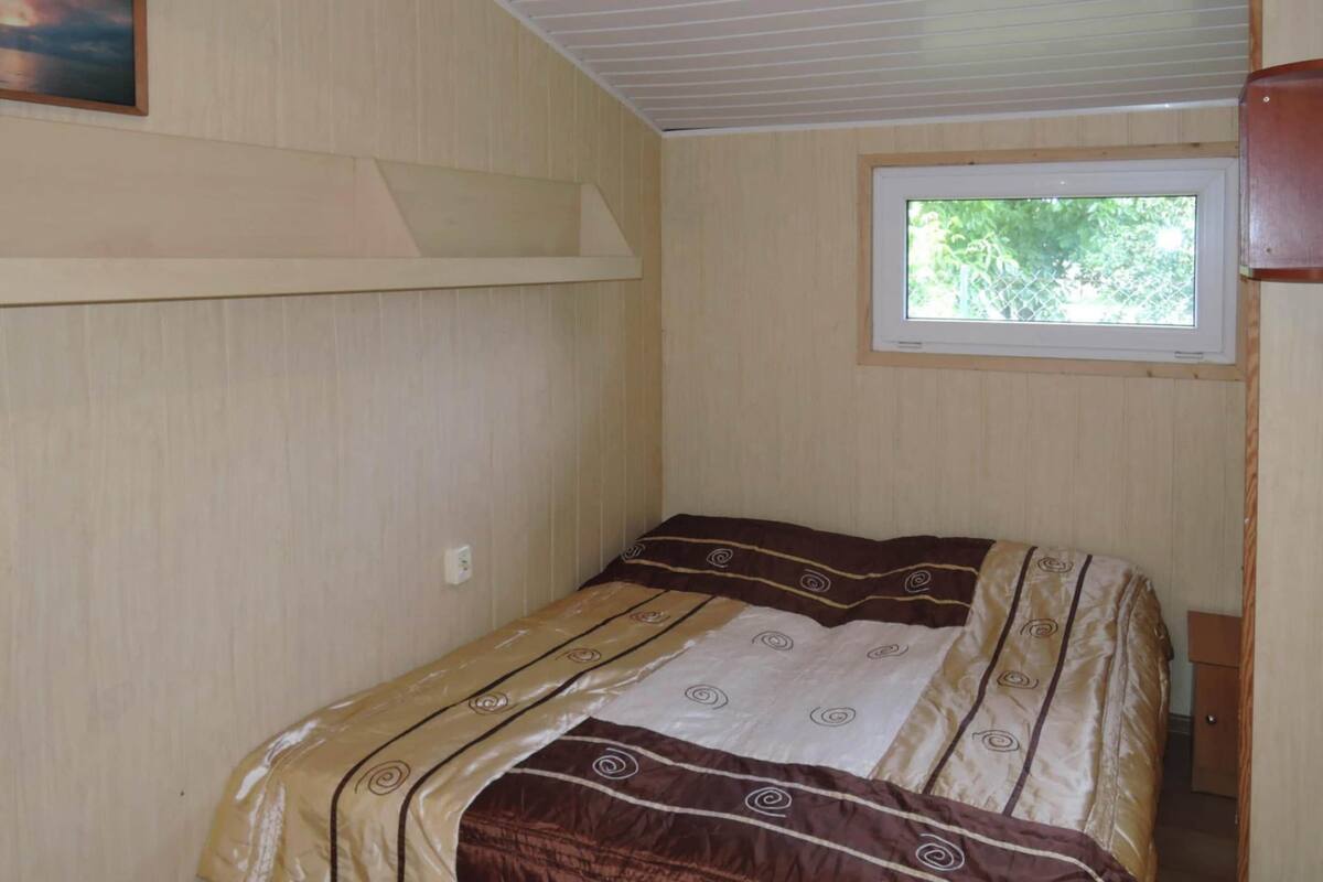 Un lit simple avec une couvre-lit à motifs, dans une pièce aux murs en bois et dotée d’une fenêtre.