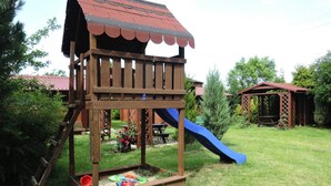 Una casita de juegos de madera con un tobogán y una pequeña plataforma llena de juguetes.