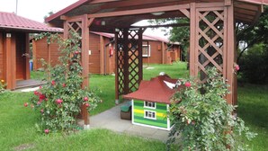 Una cabaña de madera con techo rojo, un pérgola de madera y una pequeña maqueta de casa.