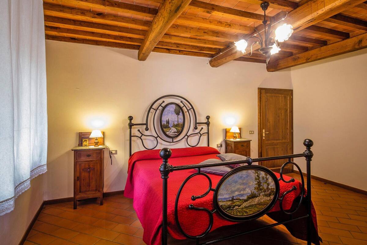 A bedroom with a wooden ceiling, a bed with a red bedspread, two bedside tables with lamps, and a wooden door.