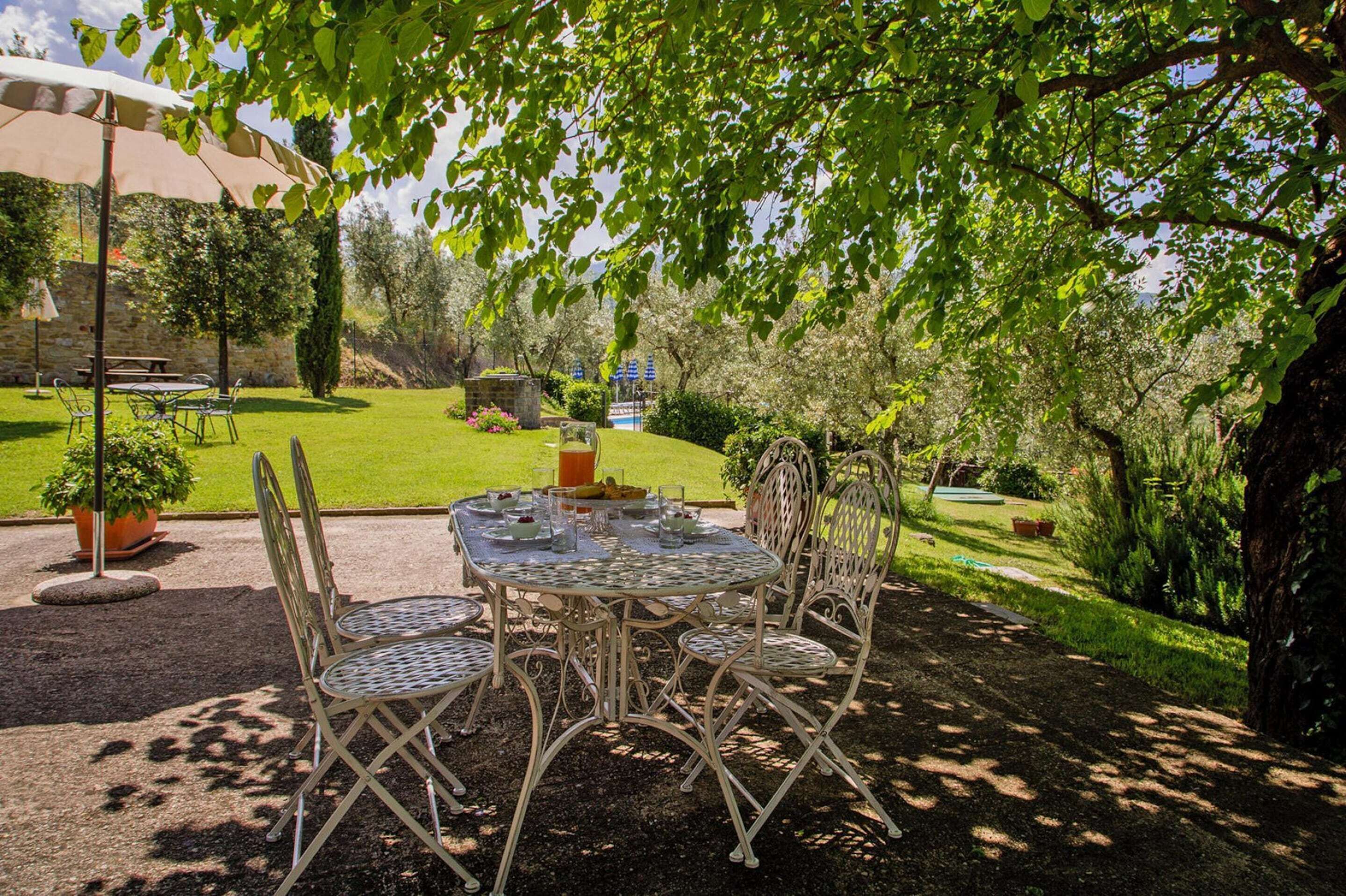 A round table with four chairs and a table umbrella in a garden setting.