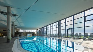 An indoor swimming pool with clear blue water, surrounded by large windows offering views of the sky and distant landscape. - Reihenhaus im Ostseeresort Dampland (Damp)