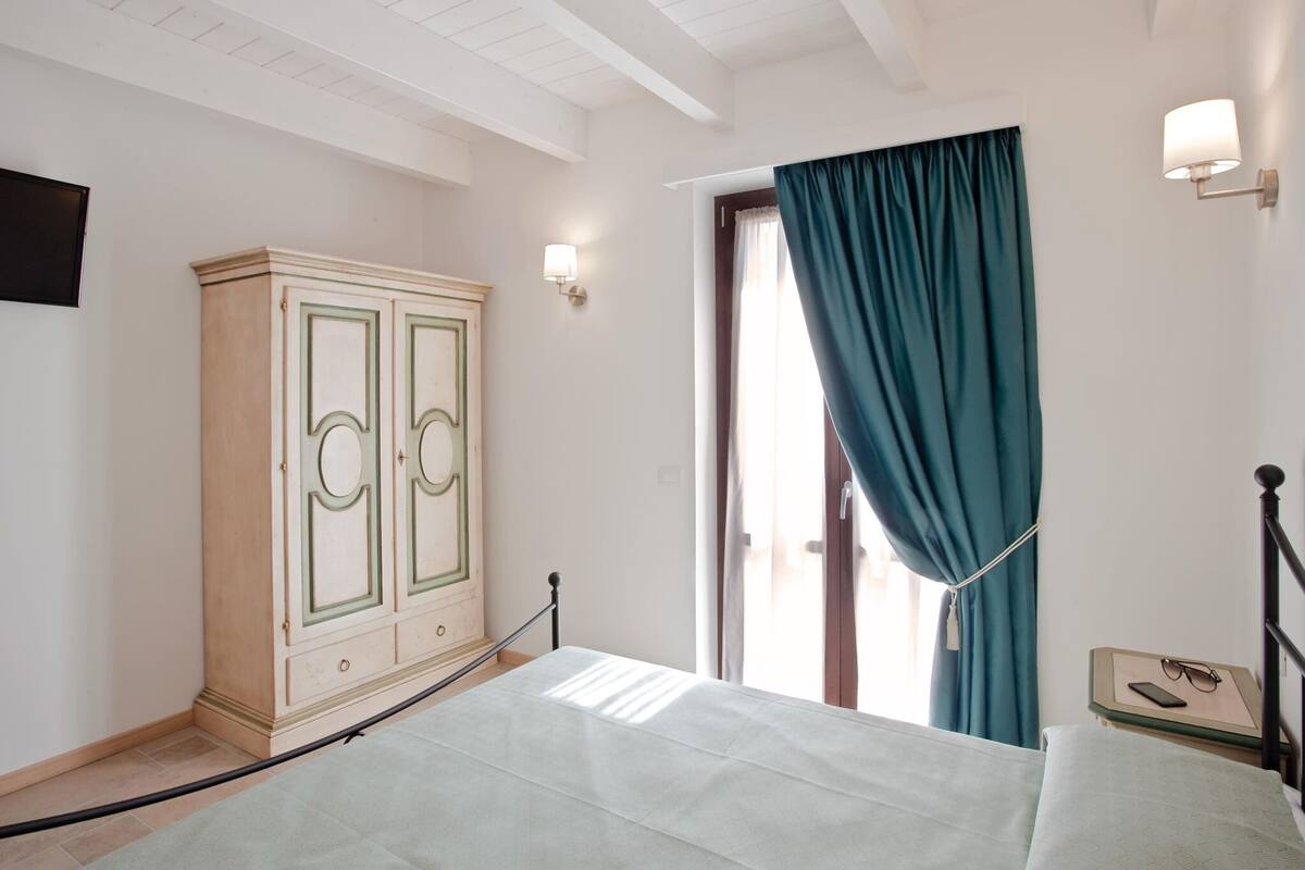 A bedroom with a bed, a wardrobe, a window with curtains, and a bedside table with a lamp.