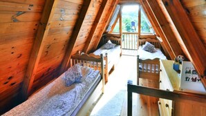 A cozy attic bedroom with wooden walls and a sloped ceiling. There are two single beds with pillows and a small table with a chair. A window at the far end provides a view of the outdoors. - Holiday Home in Osieki Near a Lake (gmina Sianów)