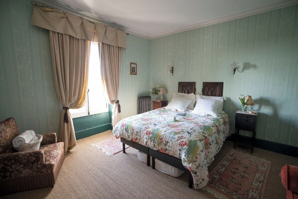 Une chambre à coucher avec un lit, une table de chevet, une chaise et une fenêtre avec des rideaux.