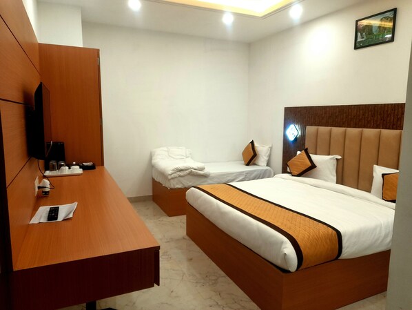 A hotel room with a wooden desk, two single beds, a large bed, and a television on the wall. - THE SHEHNAI RESORT (Alwar)