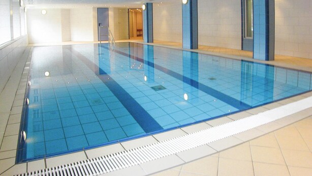An indoor swimming pool with clear blue tiles, a tiled floor, and a ladder leading to a door. - Apartment in Cuxhaven With Community Pool (Cuxhaven)