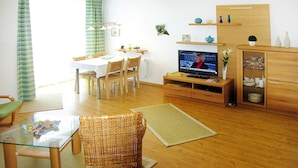 A living room with a dining area, a television, and a wooden cabinet. - Apartment in Cuxhaven With Community Pool (Cuxhaven)