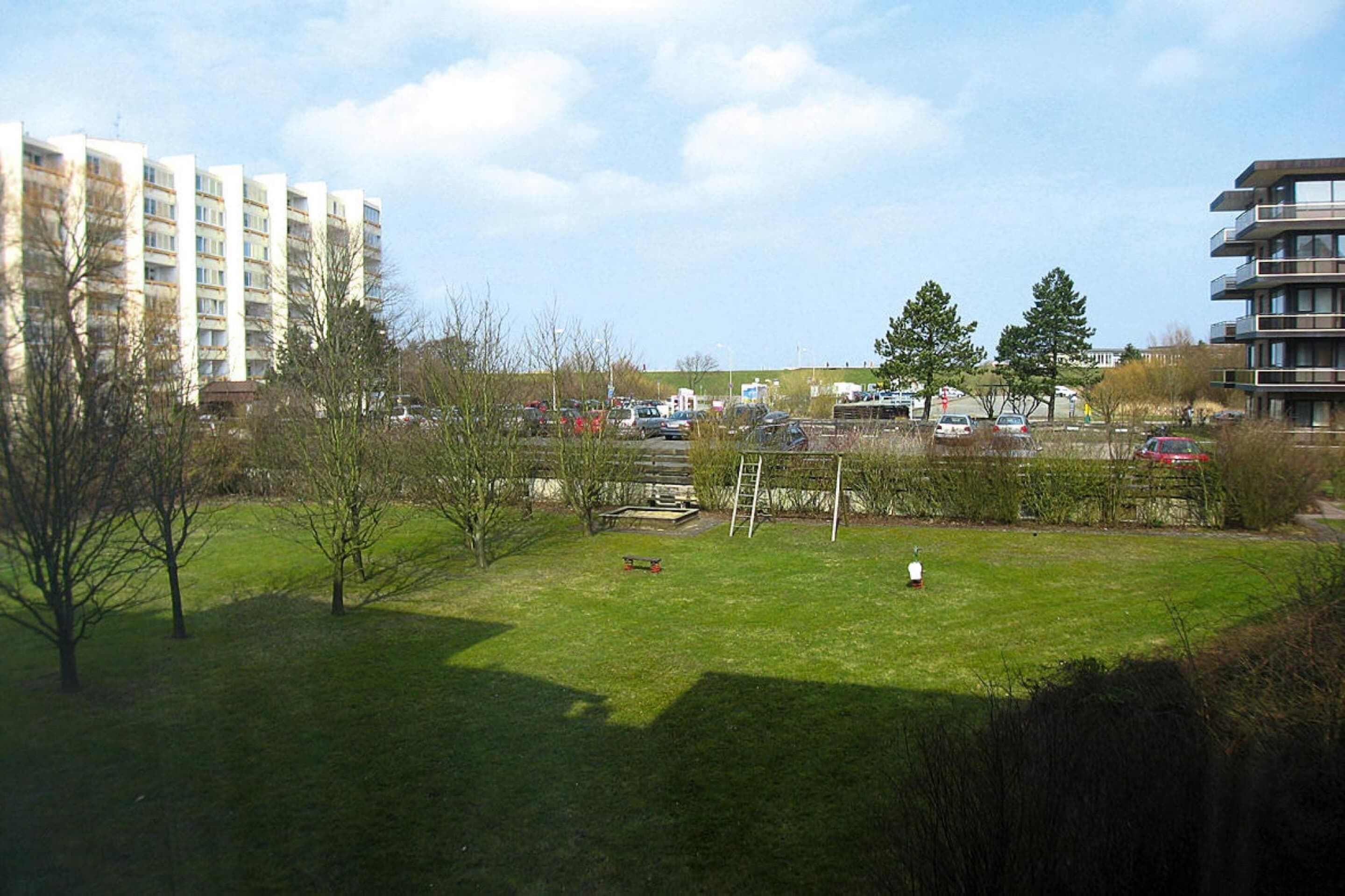 A grassy area with a soccer goal, trees, and a parking lot with cars.