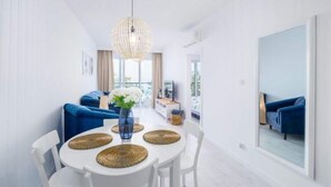 A modern dining area with a round table, white chairs, and woven placemats. - Apartment Next to the Beach With sea View, Ustronie Morskie (Ustronie Morskie)