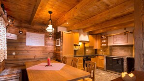 A cozy wooden cabin interior with a dining table, chairs, a kitchen area, and a fireplace. - Chalet Steinbock, St. Martin am Tennengebirge (Sankt Martin am Tennengebirge)