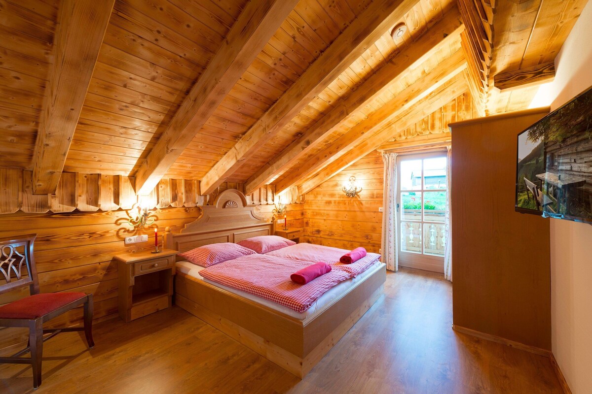 A wooden cabin bedroom with a bed, a desk, and a chair.