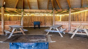 Interior rústico de madera con una parrilla, bancos y luces colgantes.