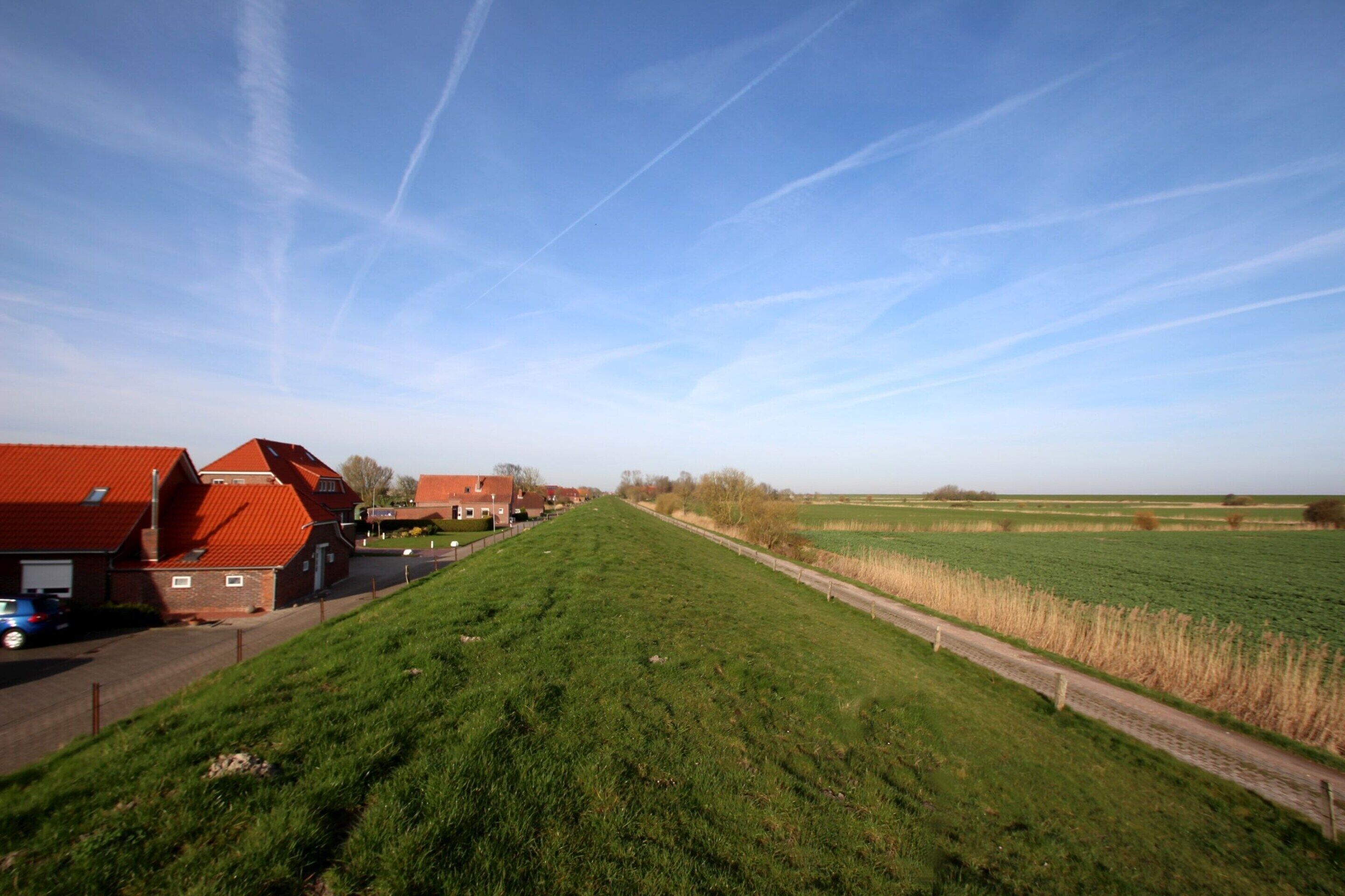 A rural landscape with a road, green fields, and red-roofed buildings.