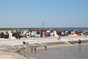 Una playa con cabañas de colores, una bandera y gente disfrutando la arena.