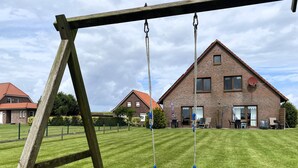 A wooden swing set in a grassy yard with a brick house in the background.