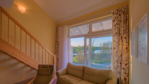 A living room with a sofa, a chair, a staircase, and a window with curtains. - Apartment in Granzow Near the Lake (Mirow)