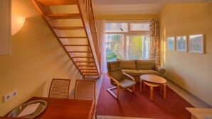 A room with a wooden staircase, a sofa, a chair, a small table, and a window with curtains. - Apartment in Granzow Near the Lake (Mirow)