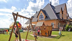 Ein Spielplatz mit Schaukeln und einer Kletterkonstruktion vor einem Haus mit Satteldach.