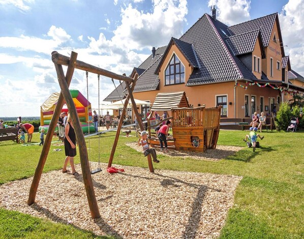A playground with swings and a climbing structure in front of a house with a sloped roof.