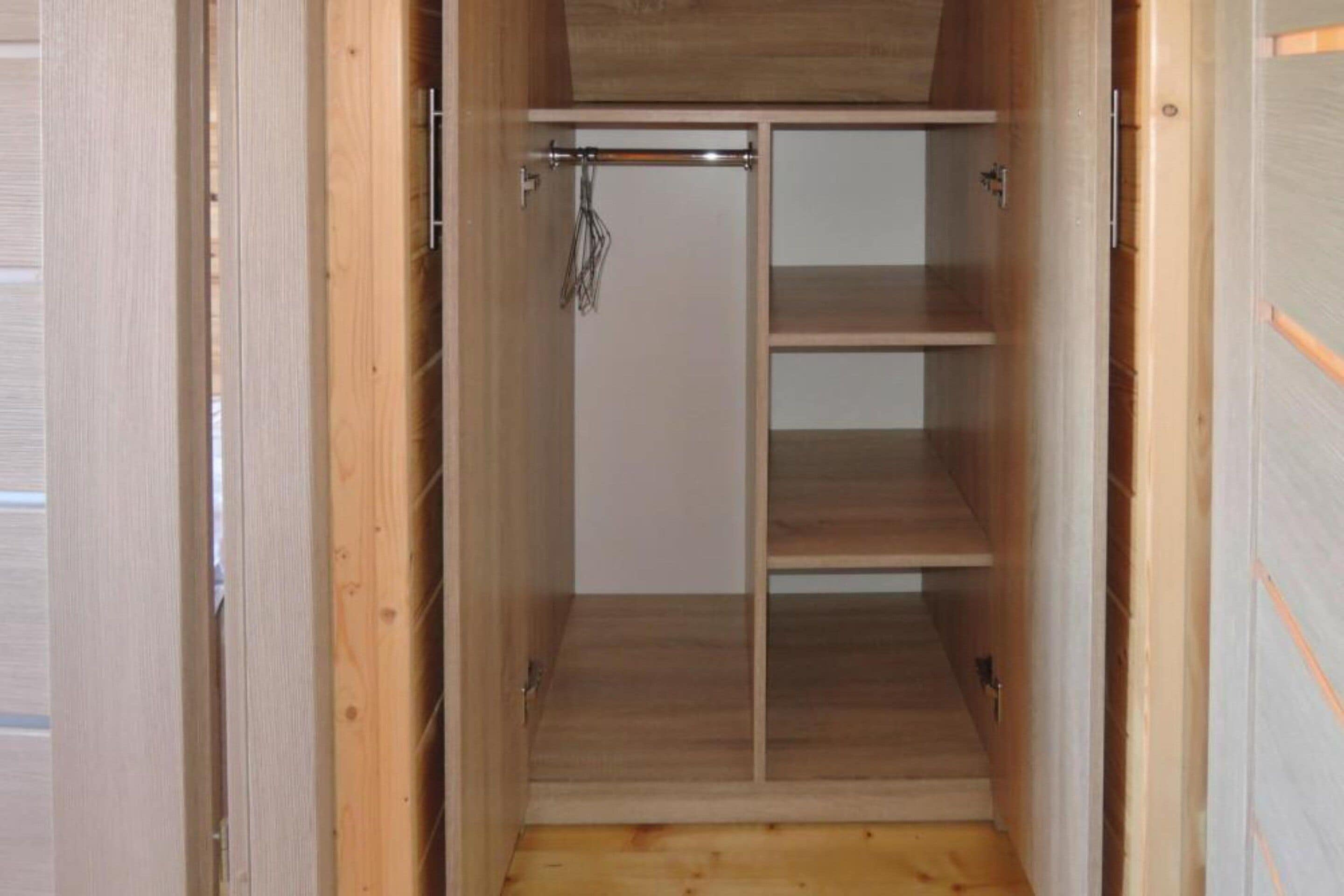 A wooden closet with a sliding door and multiple shelves.