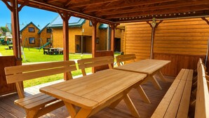 Een houten terras met picknicktafels en banken, met uitzicht op een gazon met huizen op de achtergrond.