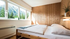 A bedroom with a wooden bed, large windows, a radiator, and a view of mountains.