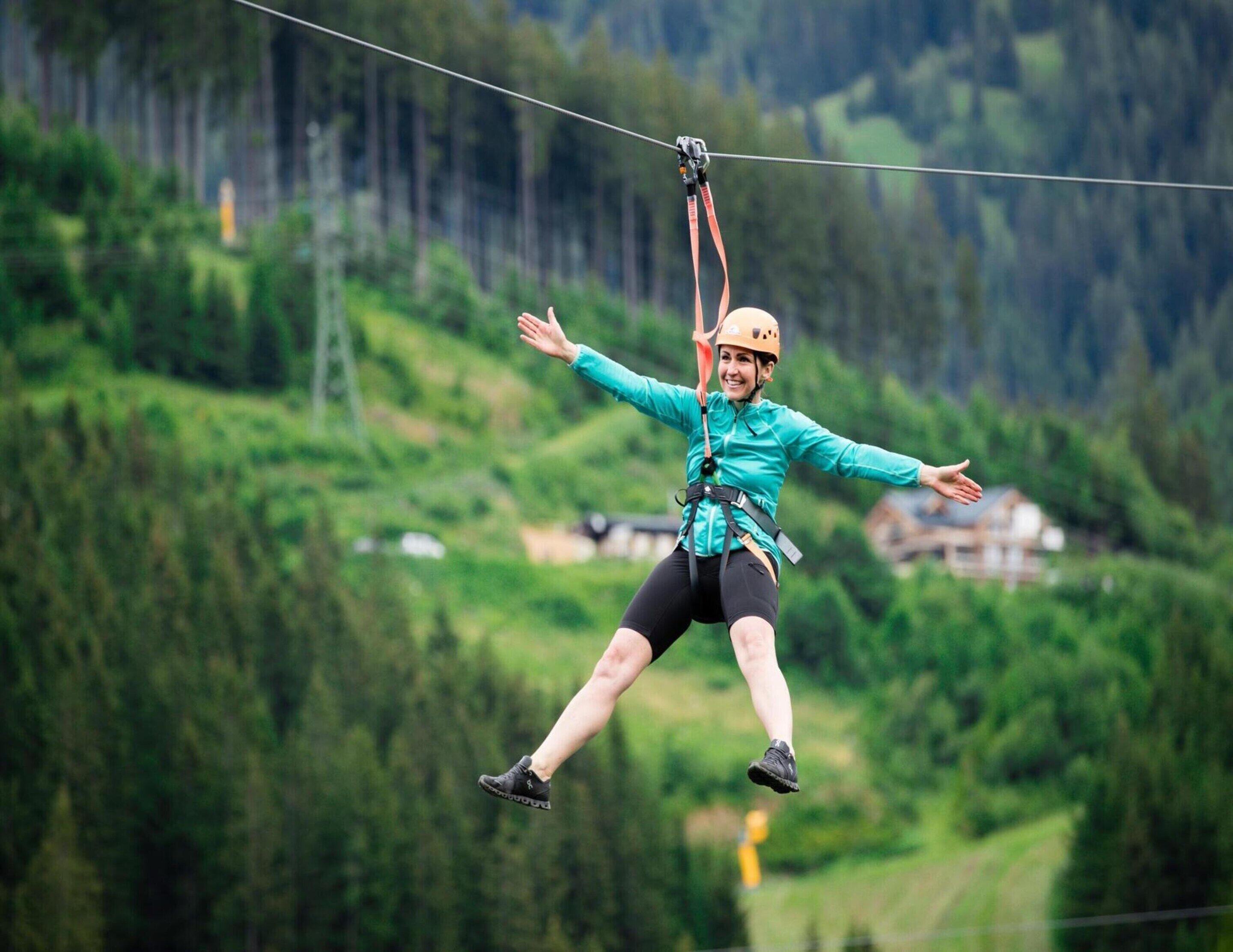 A person zip-lining with a harness and helmet, surrounded by a mountainous landscape.