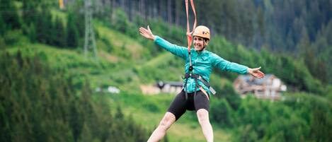 A person zip-lining with a harness and helmet, surrounded by a mountainous landscape.