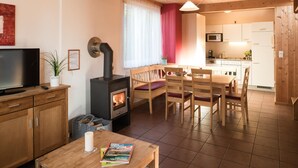 A cozy living area with a TV, a fireplace, a dining table, and a kitchen in the background.