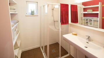 A bathroom with a glass shower enclosure, a white sink, and a red towel.