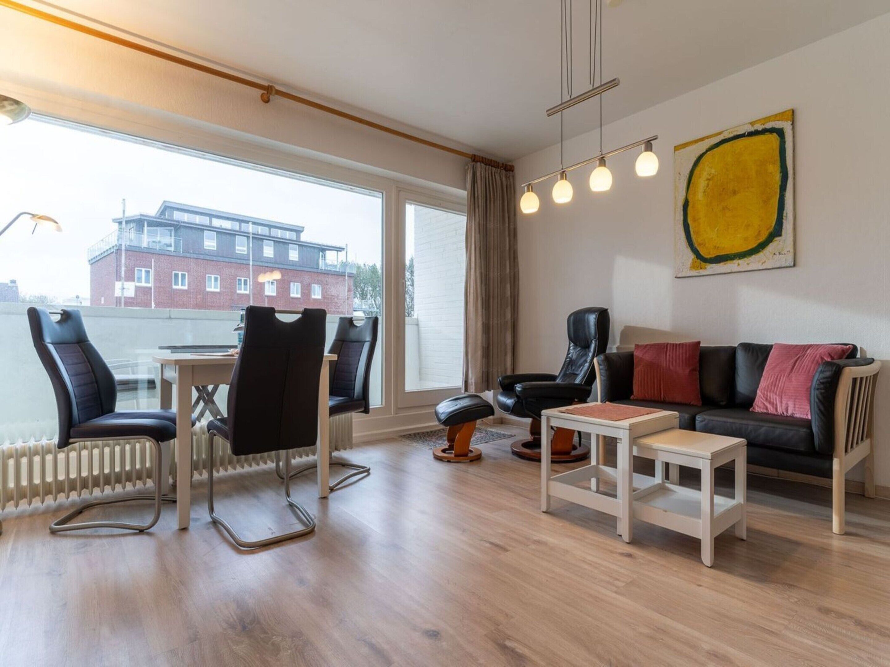 A modern living room with a view of a building through large windows, a black leather sofa, a white coffee table, and a black leather chair.