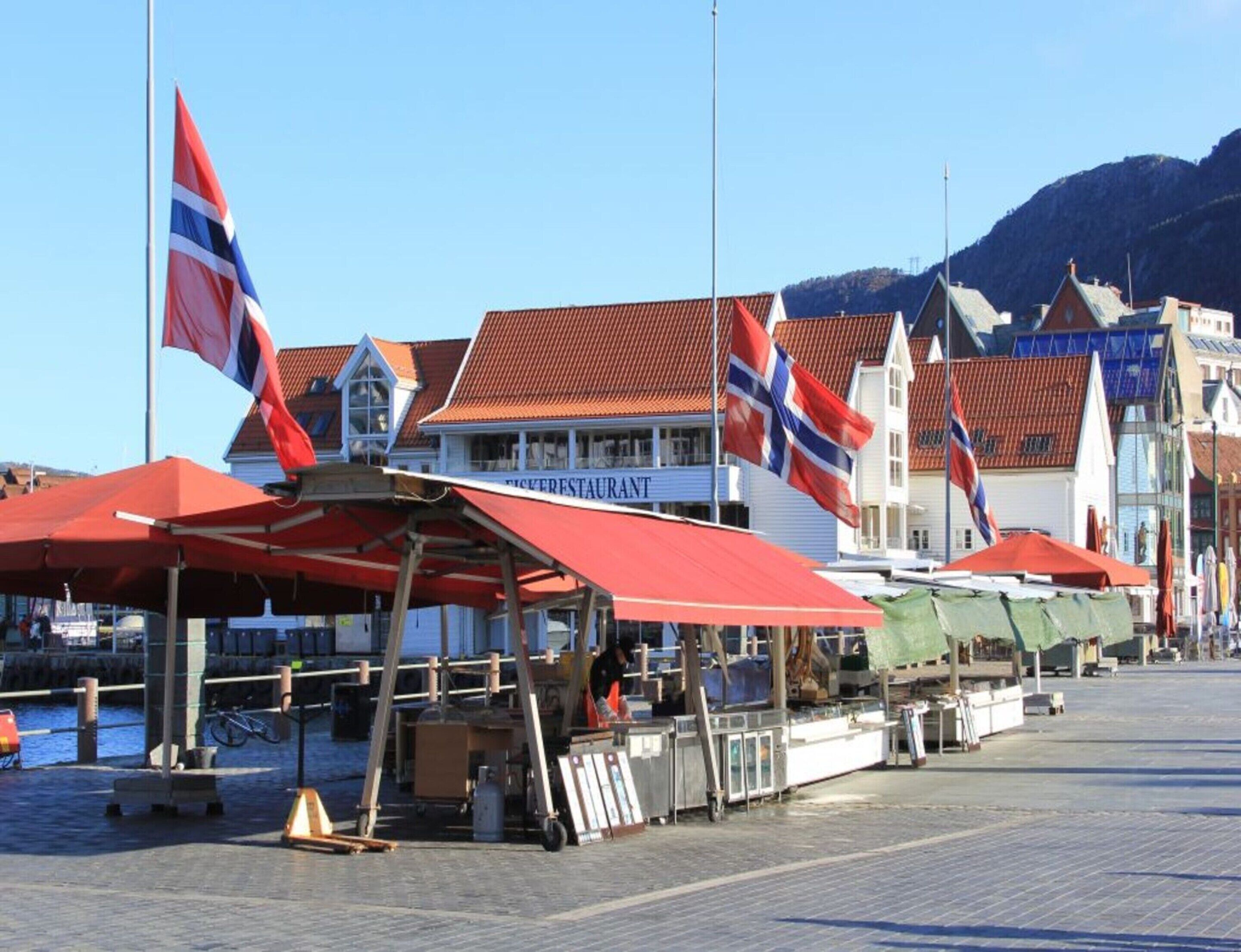 A waterfront area with red canopies, a restaurant, and buildings with red roofs.