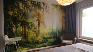 A bedroom with a forest mural, a white chair, and a large window. - Ferienwohnung Hexenzauber I und II in Braunlage (Braunlage)