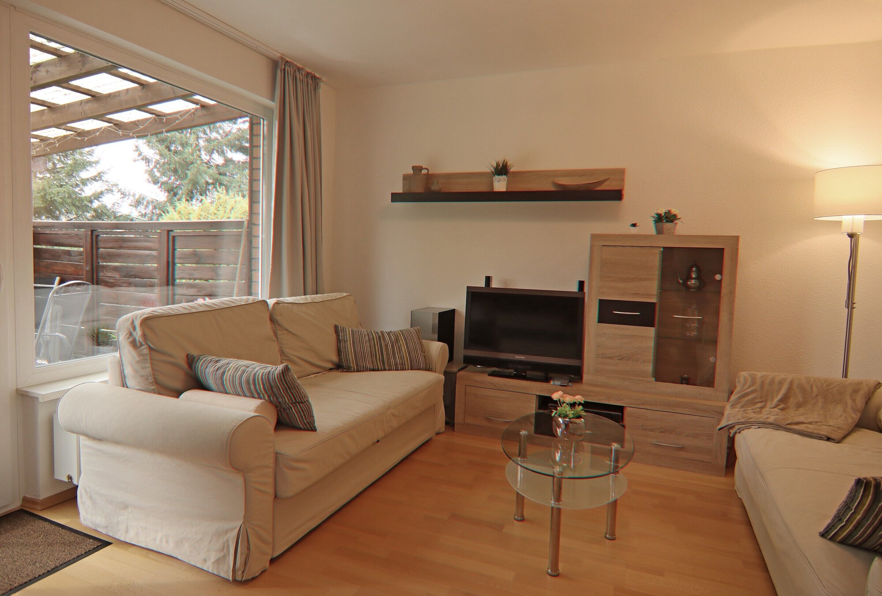 A living room with a sofa, a glass coffee table, a TV, and a wooden cabinet.