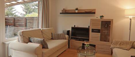 A living room with a sofa, a glass coffee table, a TV, and a wooden cabinet.