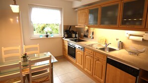A modern kitchen with wooden cabinets, a dishwasher, a sink, and a dining area with a glass table and chairs. - Ferienwohnung Hexenzauber I und II in Braunlage (Braunlage)