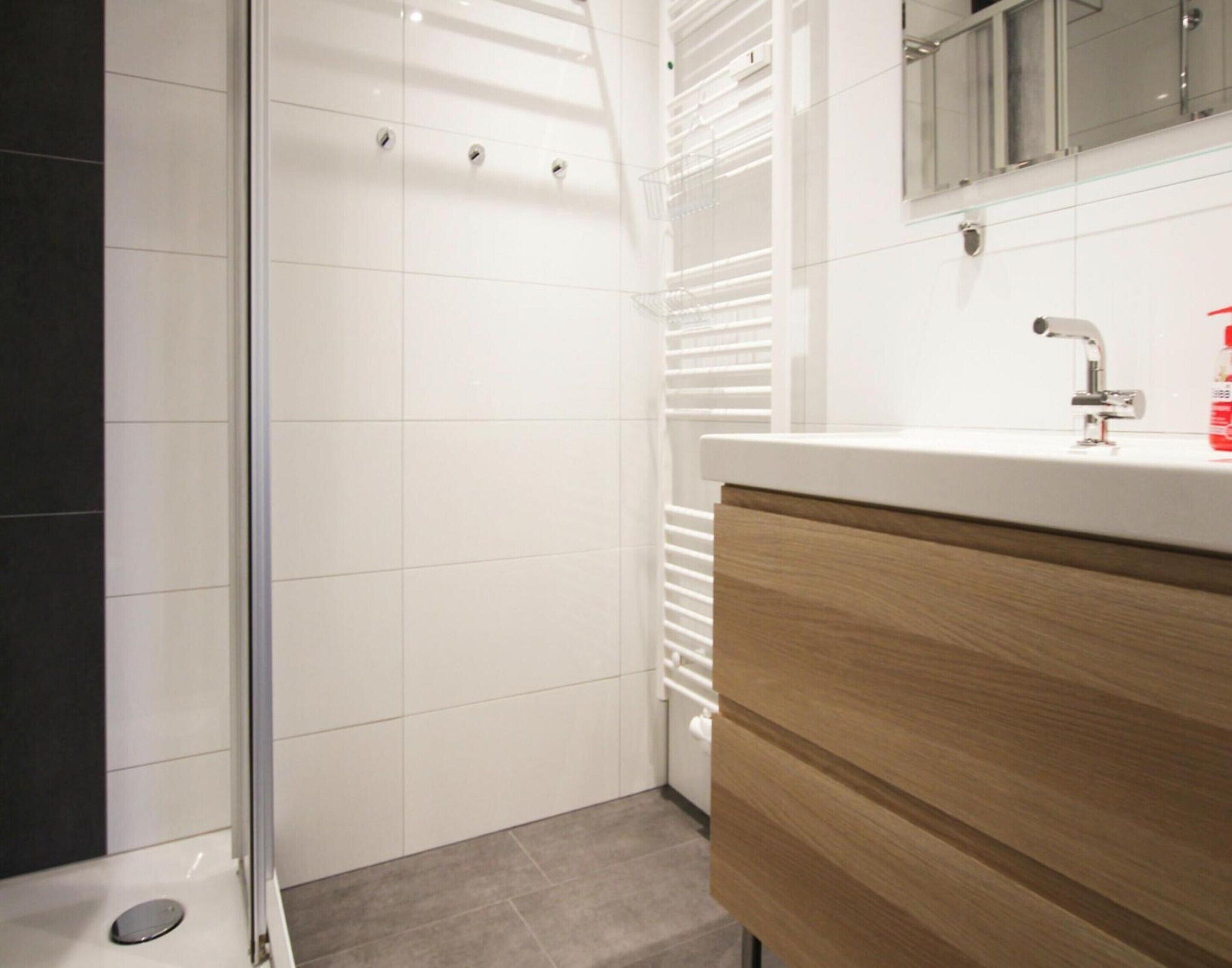 A modern bathroom with a glass shower enclosure, a white sink with a wooden cabinet, and a mirror above the sink.