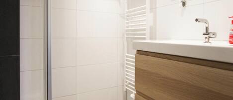 A modern bathroom with a glass shower enclosure, a white sink with a wooden cabinet, and a mirror above the sink.