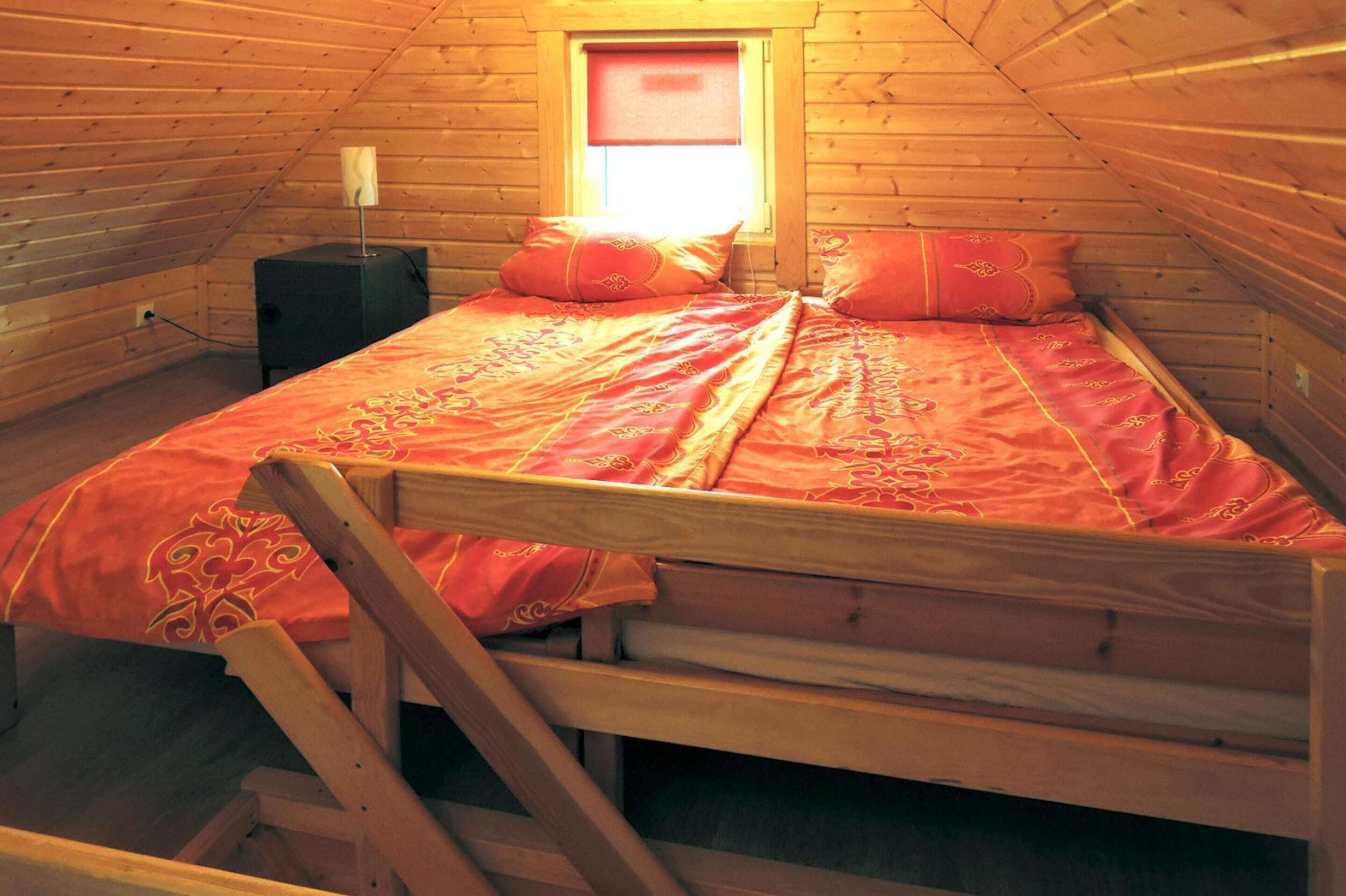 Un dormitorio de cabaña de madera con una cama individual, una mesita de noche y una ventana con persiana roja.