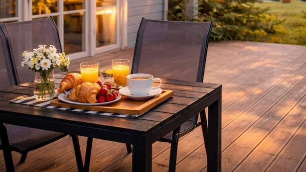 Een houten terras met een ontbijttafel, compleet met croissants, fruit en koffie.